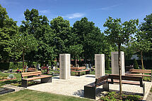 Die neuen Urnenstelen auf einem quadratischen Platz mit Bänken und neu gepflanzten Bäumen